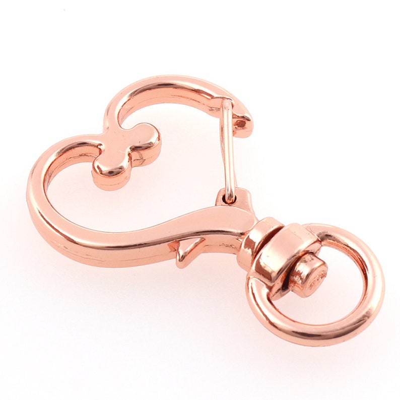 May include: Rose gold heart-shaped swivel clasp with a round ring. This metal clasp is perfect for attaching to keychains, bags, or other accessories.