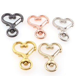 May include: Five heart-shaped keychains with a swivel clasp. The keychains are in black, rose gold, silver, gold, and brass.