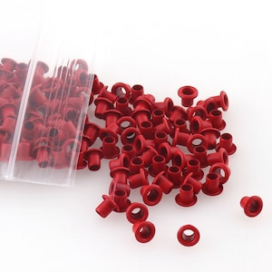 Puede incluir: Un montón grande de ojales de metal rojo, comúnmente utilizados para manualidades y trabajos en cuero.