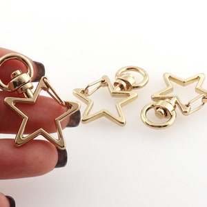 May include: Three gold-tone star-shaped keychains with swivel clasps. Each keychain features a star-shaped loop and a round swivel clasp.