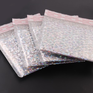 May include: Five silver iridescent padded mailing envelopes with a red warning label that reads "REMOVE TO EXPOSE ADHESIVE" on each envelope.
