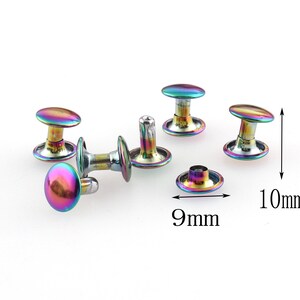 Puede incluir: Un conjunto de cinco remaches metálicos iridiscentes, cada uno con una parte superior abovedada y una base plana. Los remaches tienen un diámetro de 9 mm y una altura de 10 mm.