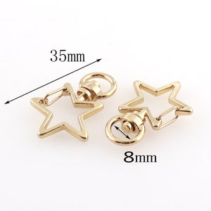 May include: Two gold-tone star-shaped keychains with swivel clasps. The keychain on the left measures 3.5 inches in length. The keychain on the right measures 0.8 inches in diameter.