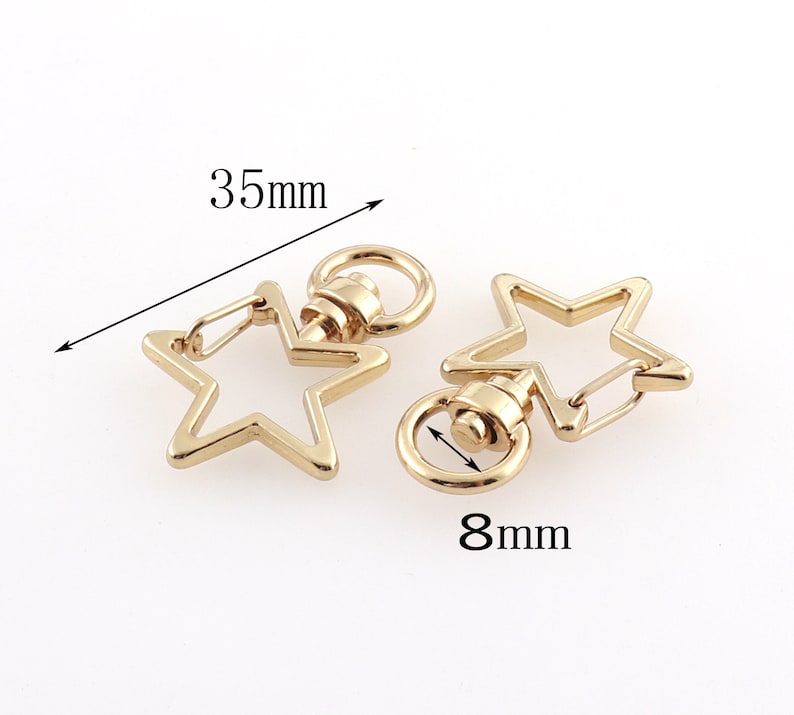 May include: Two gold-tone star-shaped keychains with swivel clasps. The keychain on the left measures 3.5 inches in length. The keychain on the right measures 0.8 inches in diameter.