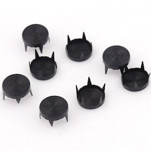 Può includere: Otto borchie in metallo nero con base circolare e cinque punte appuntite. Le borchie hanno un design a cerchi concentrici.