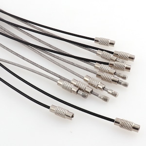 Puede incluir: Primer plano de un conjunto de llaveros plateados y negros con cierres metálicos. Los llaveros están hechos de un cable delgado y flexible.