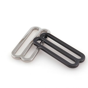 May include: Two metal slider buckles, one silver and one black. The buckles are designed for attaching straps or belts.