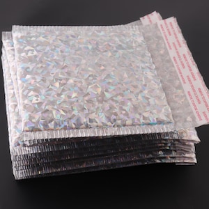 May include: A stack of silver and iridescent bubble mailers with a red adhesive strip that reads "REMOVE TO EXPOSE ADHESIVE".