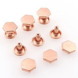 May include: Eight rose gold hexagonal metal studs, some with a raised center post. These studs are commonly used for leather crafting and DIY projects.