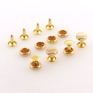 Peut inclure: Assortiment de boutons-pression en métal doré de différentes tailles et styles. Les boutons-pression sont disposés sur une surface blanche.