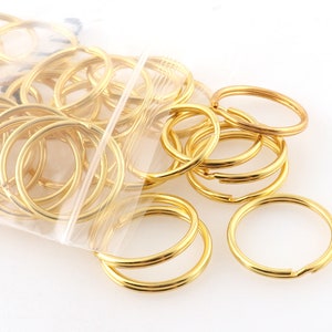 May include: A close-up of a bag filled with gold-colored metal key rings. The key rings are various sizes and are arranged in a random pattern.