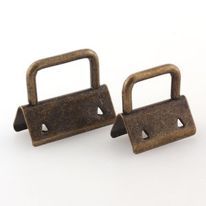 May include: Two antique gold-toned metal D-ring clasps. The larger clasp is about 2 inches wide and the smaller clasp is about 1.5 inches wide.