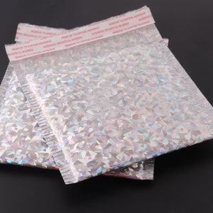 May include: Two silver iridescent padded mailing envelopes with a red adhesive strip that reads "REMOVE TO EXPOSE ADHESIVE".