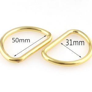 以下が含まれることがあります： 金色の金属製のDリングが2つ。大きい方のリングは直径50mm、小さい方のリングは直径31mmです。