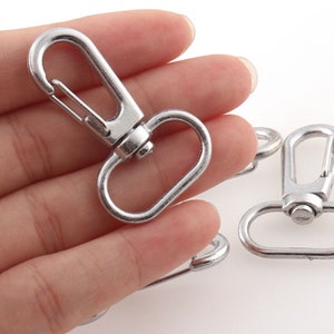 May include: Silver metal swivel clasps with a spring-loaded gate. The clasps are designed for attaching to straps, leashes, or other items.