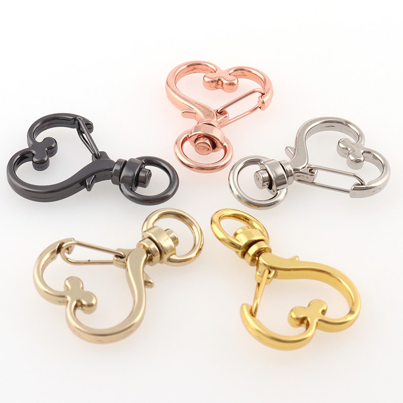 May include: Four heart-shaped metal keychains in different finishes: black, rose gold, silver, and gold. Each keychain features a spring-loaded clasp and a swiveling ring.