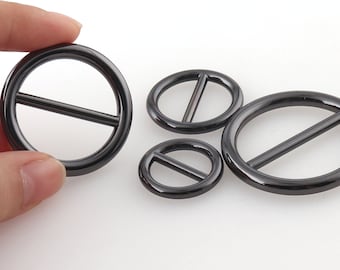 May include: Four black metal ring buckles of different sizes. The buckles have a smooth, shiny finish and a simple, minimalist design.