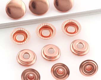 May include: A collection of copper-colored snap fasteners. The image shows the top and bottom parts of the snaps, with the top pieces being smooth and rounded, and the bottom pieces having a circular design with a central hole.