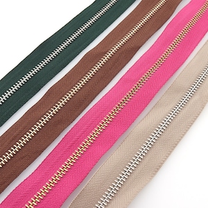 May include: Five different colours of zipper tape with gold and silver metal teeth. The colours are green, brown, pink, beige, and white.