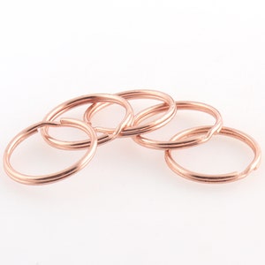 May include: Five rose gold key rings, stacked on top of each other. The key rings are made of metal and have a smooth finish.