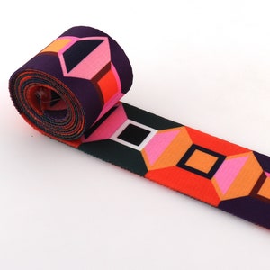 May include: Rolled-up patterned fabric with a geometric design in shades of purple, pink, orange, and black. The fabric is unrolled to reveal the repeating pattern of diamonds and squares.