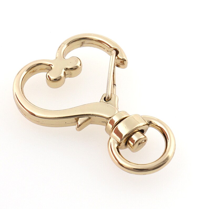 May include: Gold-toned metal heart-shaped swivel clasp with a spring-loaded gate. The clasp has a round ring on the bottom.