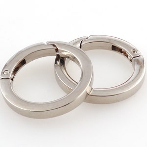 Puede incluir: Dos llaveros de metal plateado con cierre de resorte. Los anillos están entrelazados.