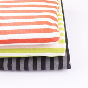 May include: Three striped fabric swatches stacked on top of each other. The top swatch is white and orange, the middle swatch is white and green, and the bottom swatch is black and gray.