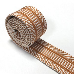 Puede incluir: Un rollo de cinta tejida blanca y naranja con un patrón geométrico. La cinta tiene aproximadamente 2,5 cm de ancho.