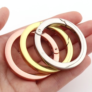 Könnte beinhalten: Drei Schlüsselringe aus Metall in verschiedenen Farben: Roségold, Gold und Silber. Die Ringe sind alle offen und haben einen federbelasteten Verschluss.
