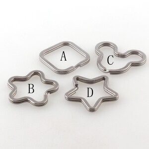 May include: Four silver keychains in different shapes: square, star, flower, and Mickey Mouse. The keychains are labeled A, B, C, and D.