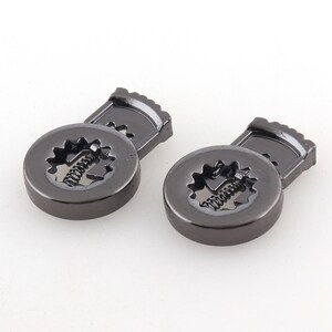 Puede incluir: Dos cierres de metal negro con un mecanismo de resorte. Los cierres están diseñados para usarse para sujetar ropa u otros artículos.