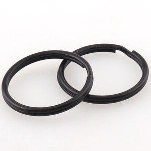 Könnte beinhalten: Zwei schwarze Schlüsselringe aus Metall, jeder mit einem Doppelring-Design.