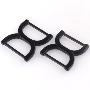 May include: Two black metal D-ring buckles. The buckles are designed to be used for straps or belts.