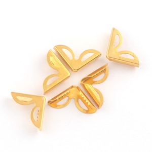 Può includere: Angolari in metallo color oro. Queste staffe a forma di L hanno un design decorativo traforato e sono ideali per proteggere gli angoli di scatole, cornici o altri progetti artigianali. L'hardware è mostrato su sfondo bianco.