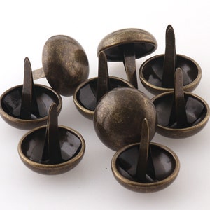 Peut inclure: Gros plan d'un groupe de clous en laiton antique en forme de dôme avec une pointe pointue. Les clous sont disposés de manière aléatoire sur une surface blanche.