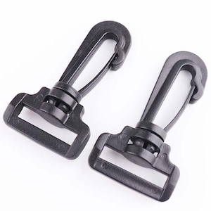 May include: Two black plastic swivel hooks with a rectangular base. The hooks are designed for attaching to straps or other materials.