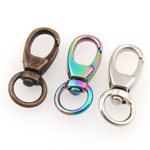 May include: Three metal swivel clasps in different finishes: antique bronze, iridescent rainbow, and silver. Each clasp has a spring-loaded gate and a small ring for attaching to a strap or chain. These clasps are used for various crafting and jewelry projects.