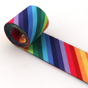 Könnte beinhalten: Gerolltes elastisches Band mit Regenbogenstreifen. Das Band besteht aus einem weichen, dehnbaren Stoff und hat ein diagonales Regenbogenstreifenmuster.