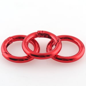 May include: Three red metal key rings with a spring-loaded clasp. The rings are interlocked.