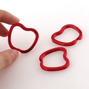 May include: Three red heart-shaped metal keychains. The keychains are made of a smooth, shiny metal.