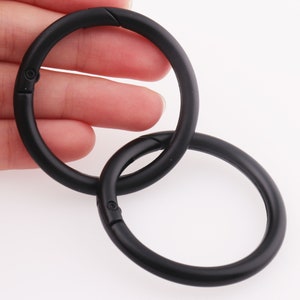 May include: Two black metal key rings with a swivel clasp. The rings are linked together.