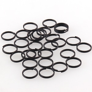 May include: A large group of black metal jump rings. The rings are all the same size and are arranged in a random pattern.