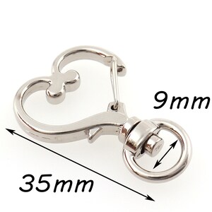 May include: Silver heart-shaped swivel clasp with a 9 mm diameter ring and a 35 mm length. The clasp is designed for attaching to a keychain, bag, or other items.