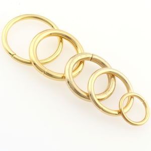 May include: A gold-colored chain link with five interlocking circular rings. The rings vary slightly in size, with the smallest at the end. The chain is made of a shiny, metallic material and is set against a white background.