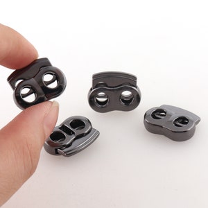 Puede incluir: Cuatro cierres de cordón de plástico negro con dos agujeros cada uno. Los cierres de cordón están diseñados para asegurar cordones o correas.