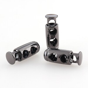 Puede incluir: Tres topes de cordón de metal negro con forma cilíndrica y tres agujeros. Los topes están diseñados para asegurar los cordones y evitar que se deshilachen.