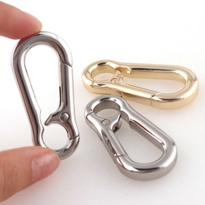 Puede incluir: Tres cierres metálicos en acabados plateado, dorado y niquelado. Cada cierre tiene una puerta con resorte y un anillo en D.