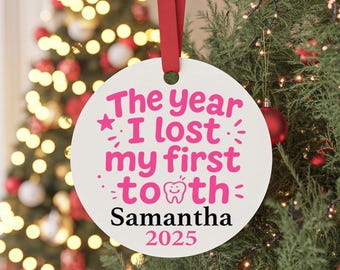 May include: A round white ornament hanging from a red ribbon. The text reads The year I lost my first tooth in pink, with a small tooth icon, followed by the name Samantha in black and the year 2025 in pink, centered on the circular surface.