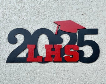 May include: Black wooden cutout of the year 2025 with a red graduation cap on top and the letters "LHS" in red in the middle.